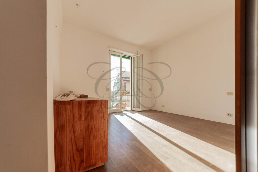 Luminosa camera da letto con balcone privato dell'appartamento venduto a Monteverde Vecchio, con pavimento in parquet e portafinestra che dà accesso allo spazio esterno.