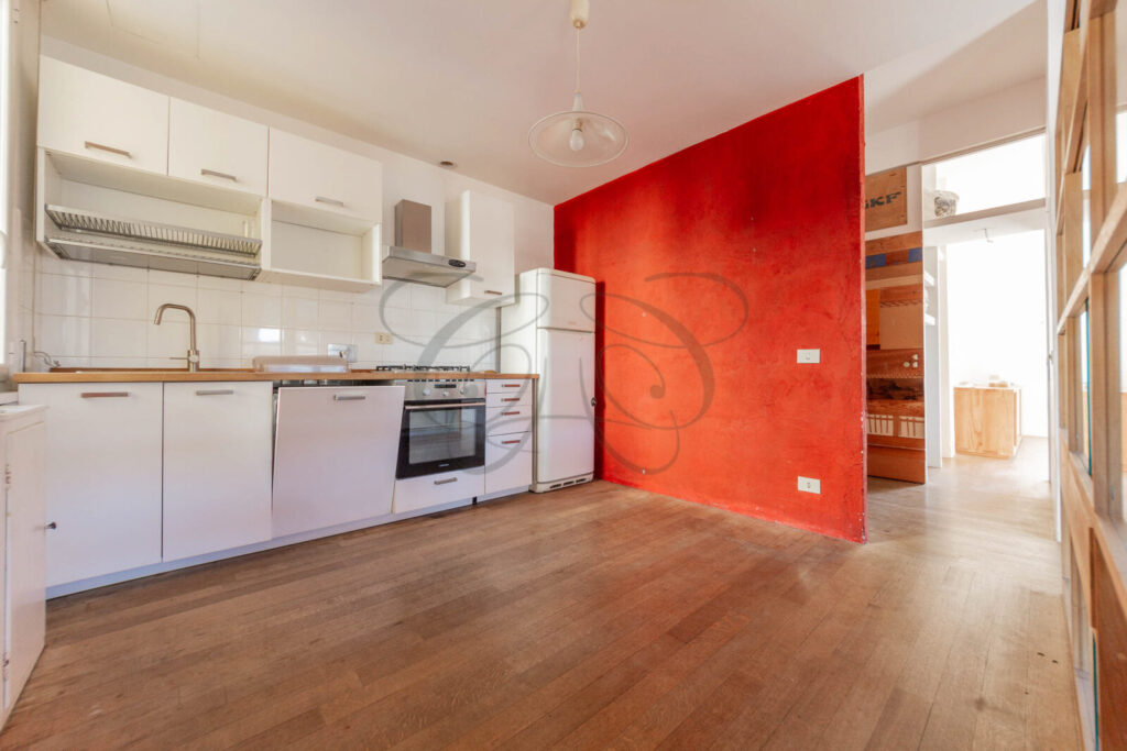 Cucina a vista moderna e attrezzata dell'appartamento venduto a Monteverde Vecchio, con parete di design rossa e pavimento in parquet.