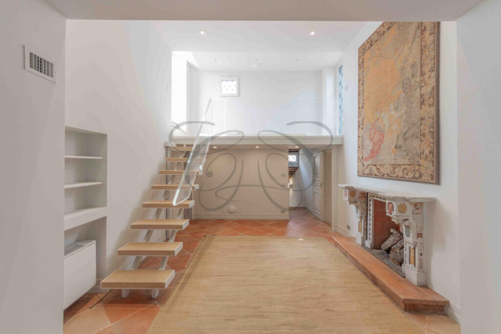 Soggiorno con soffitti a doppia altezza, un camino moderno e un ballatoio interno che si affaccia sulla zona living.