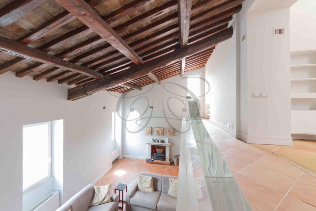 Salone di un attico di lusso a Roma con alti soffitti con travi in legno a vista e pavimento in cotto.