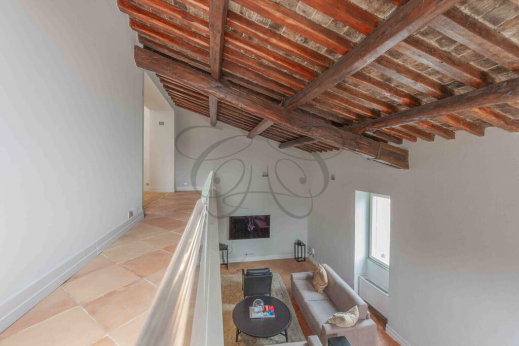 Salone di un attico di lusso a Roma con alti soffitti con travi in legno a vista e pavimento in cotto.