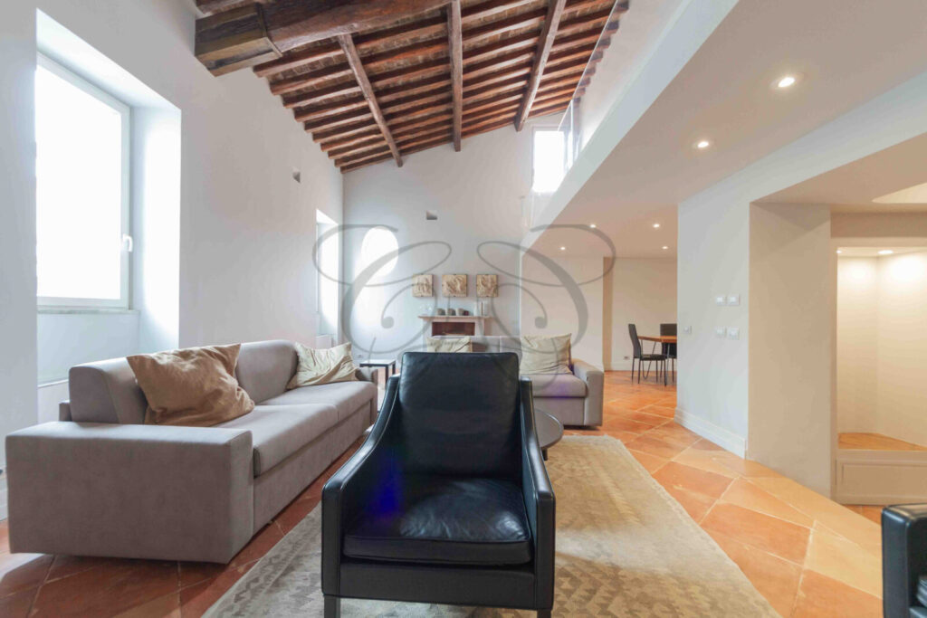 Salone di un attico di lusso a Roma con alti soffitti con travi in legno a vista e pavimento in cotto.