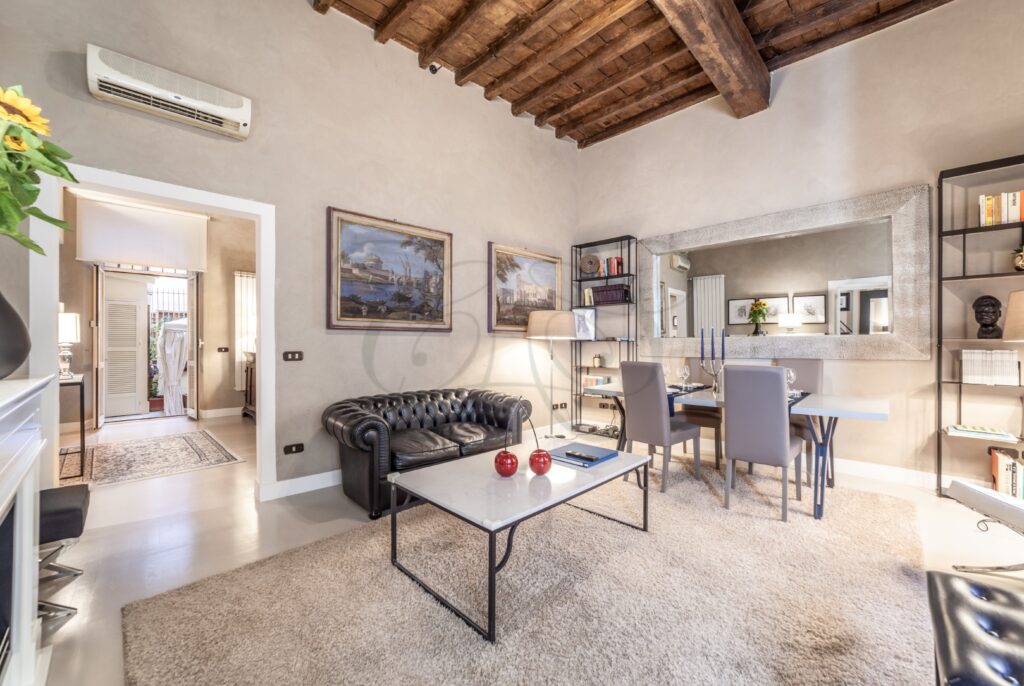 Salone di un appartamento con mobili classici e una scrivania. Le grandi finestre offrono una vista su una strada storica di Roma.