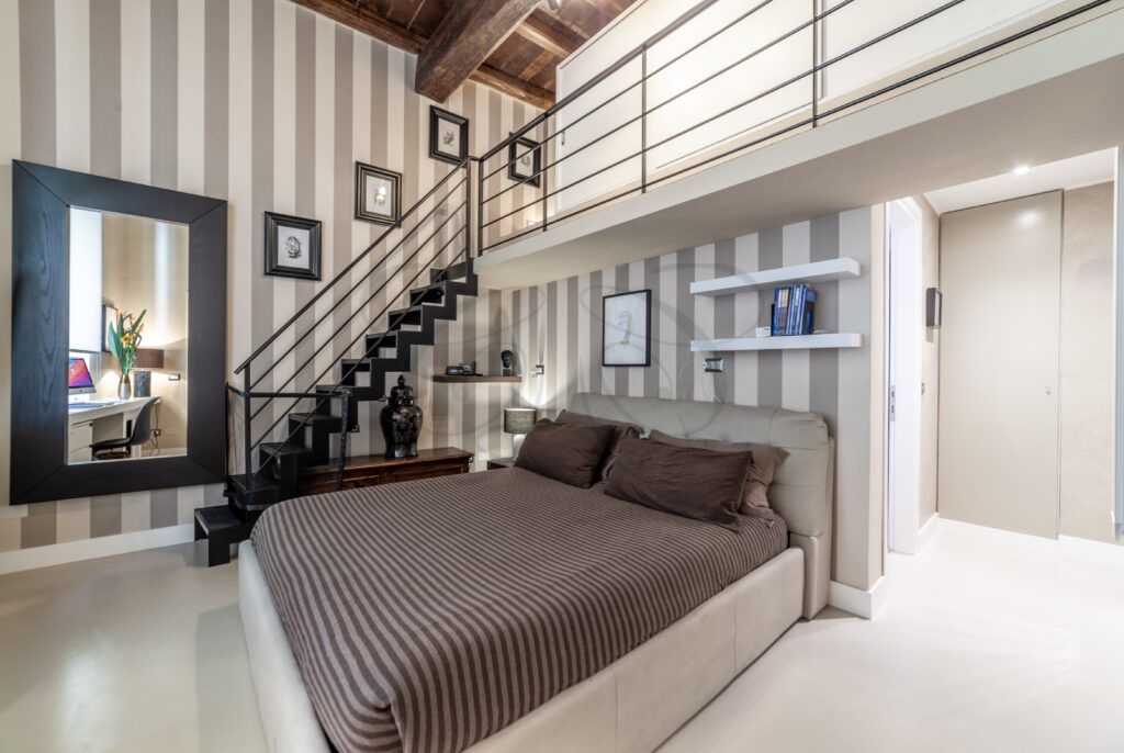 Camera da letto con soppalco, letto matrimoniale e pareti a righe. Una scala conduce al piano superiore.