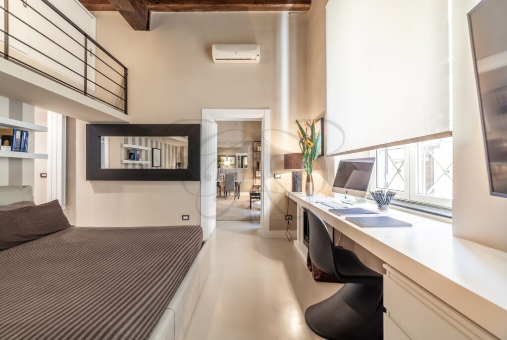 Un dettaglio di un mobile basso, uno specchio e un vaso con fiori secchi in un corridoio.