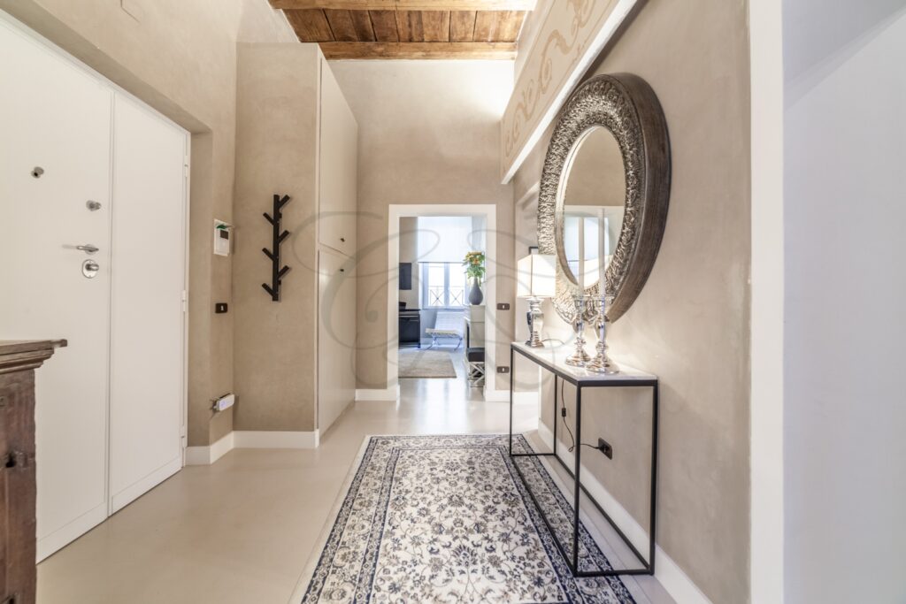 Ingresso di un appartamento di lusso a Roma, con pavimenti in parquet a spina, un grande specchio e arredi classici.