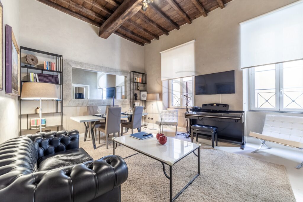 Vista frontale del salone con il camino, due ampi divani neri e un tavolino. L'ambiente è curato e ben illuminato.