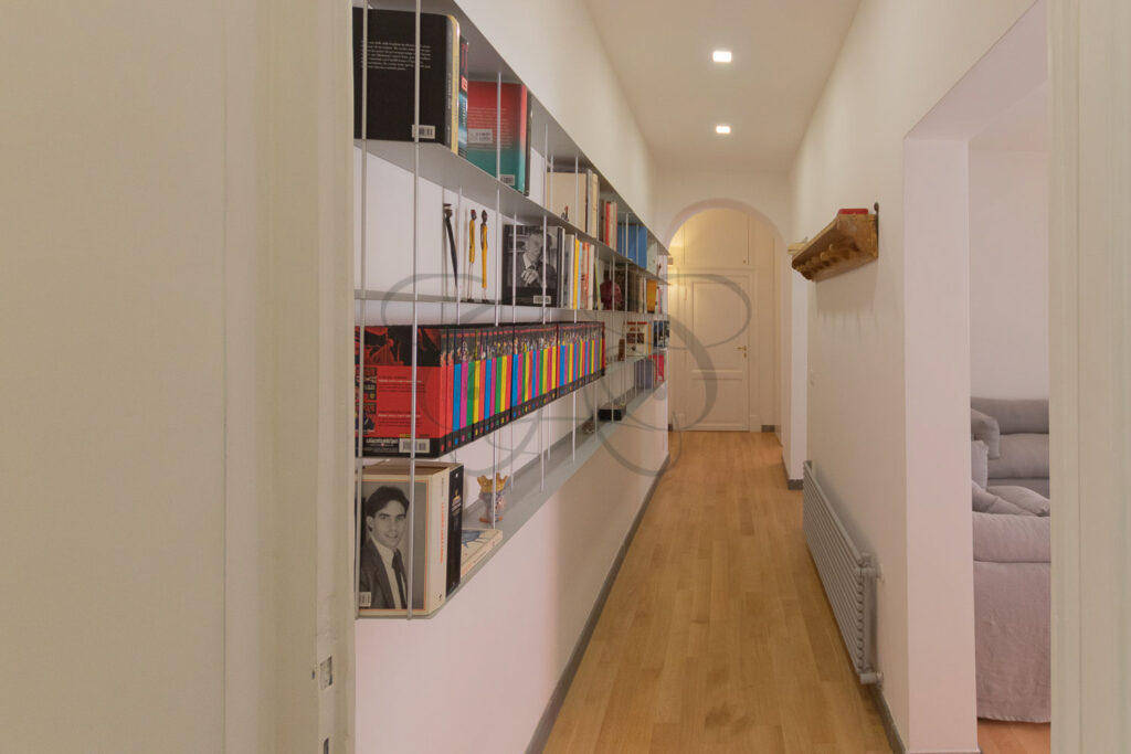 Un corridoio con una libreria bianca a muro a tutta altezza.