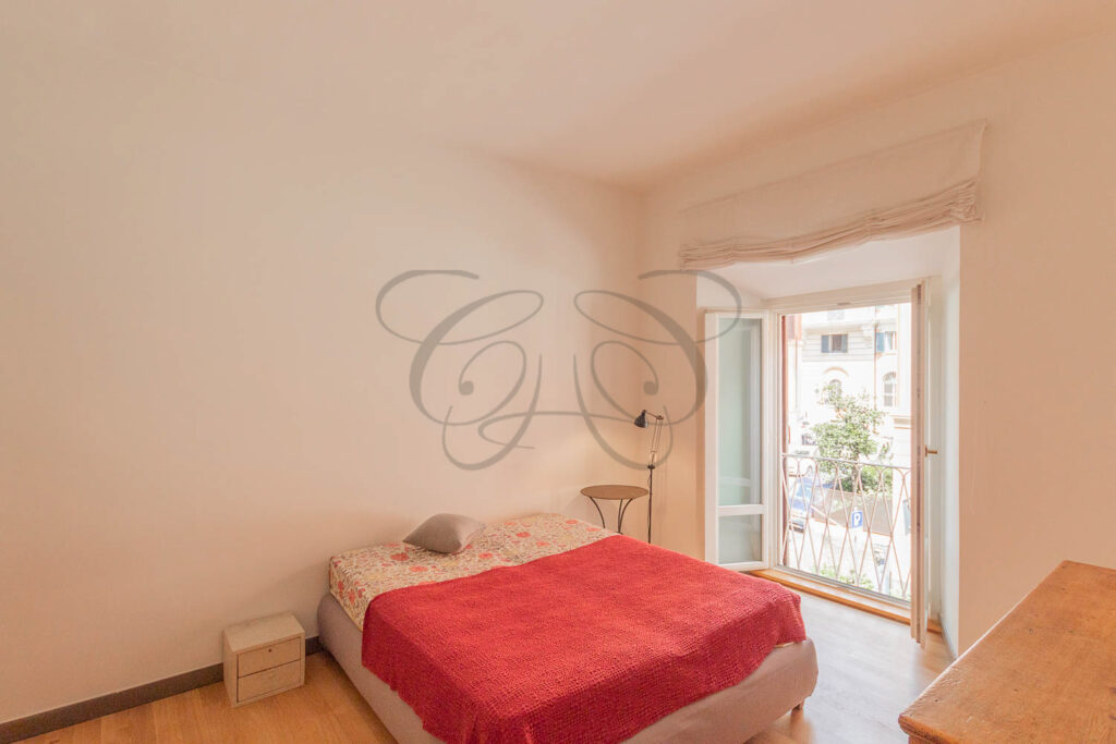 Una camera da letto con un letto matrimoniale rosso, un pavimento in parquet e una porta finestra che porta a un balcone.