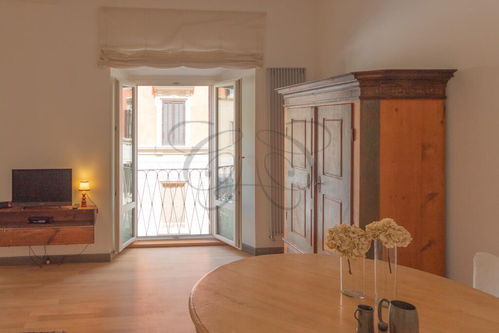 L'ambiente living con un tavolo rotondo e sedie di fronte a una porta finestra che si apre su un balcone, che rende l'ambiente luminoso.