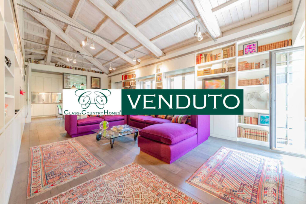 Salone luminoso con soffitto a travi bianche e divano viola nell’attico venduto in Via Giulia, Roma.