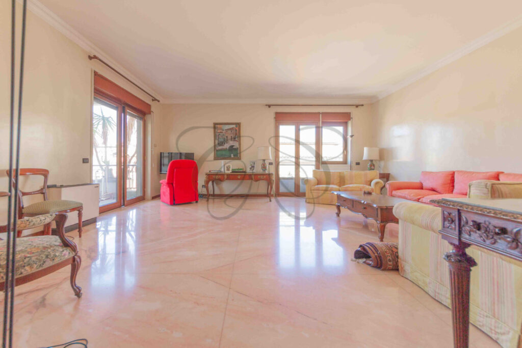 Ampio salone con pavimento in parquet, arredato con divani e poltrone rossi. Le grandi finestre illuminano l'ambiente.