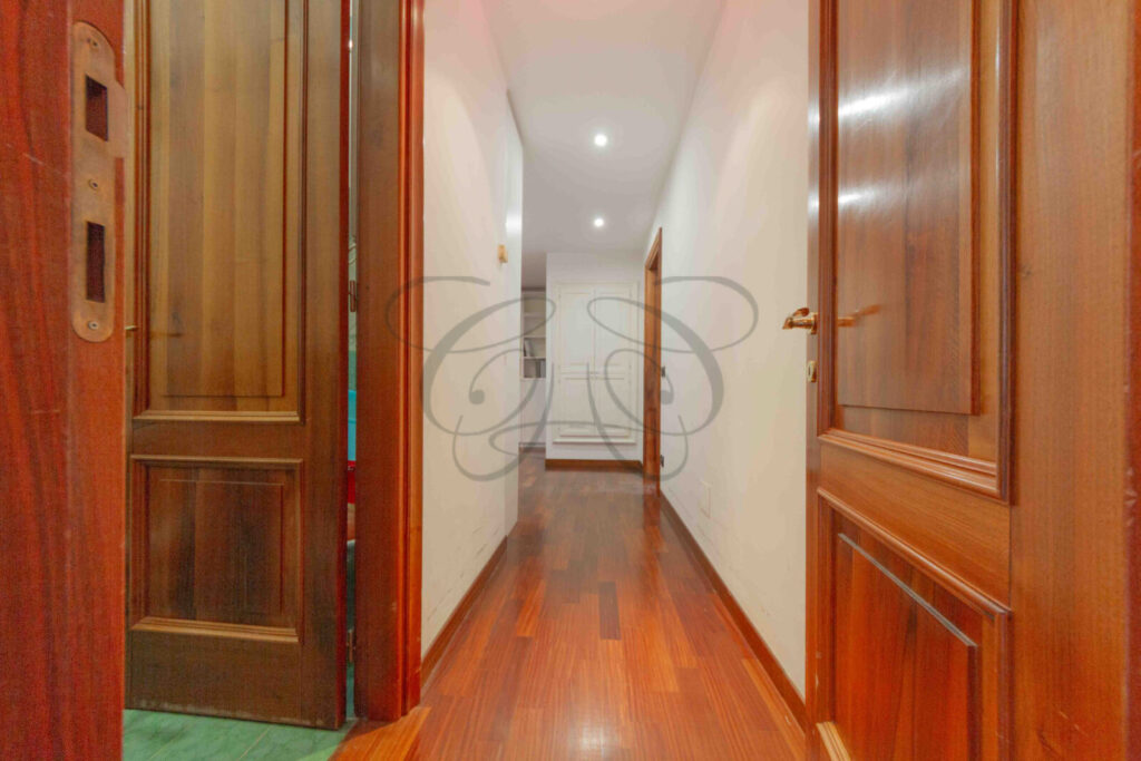 Corridoio con pavimento in parquet e un arco che conduce a un'altra stanza.