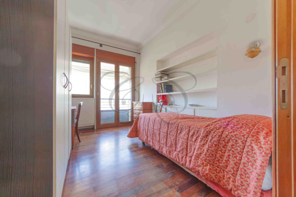 Terza camera da letto con un letto, un comodino e una sedia. La luce naturale entra dalla finestra.