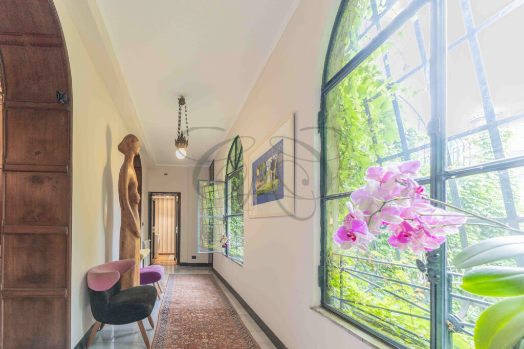 Elegant hallway with large arched windows, wooden sculpture, and orchids, penthouse for rent Rome historic center.