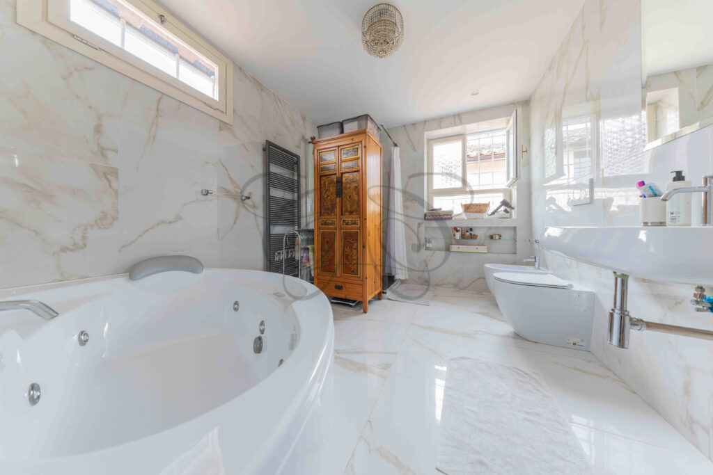 Bagno lussuoso con vasca idromassaggio ovale, rivestimenti in marmo e mobile antico, attico in affitto Roma.
