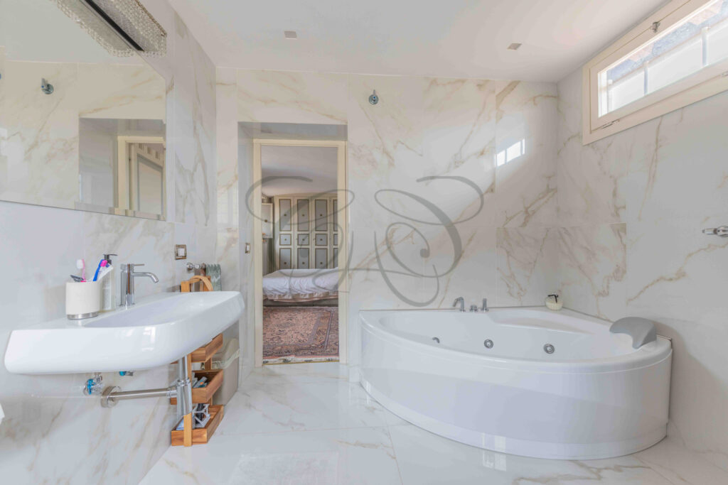 Bathroom with corner jacuzzi tub, modern sink, and view into the bedroom, penthouse for rent Rome.