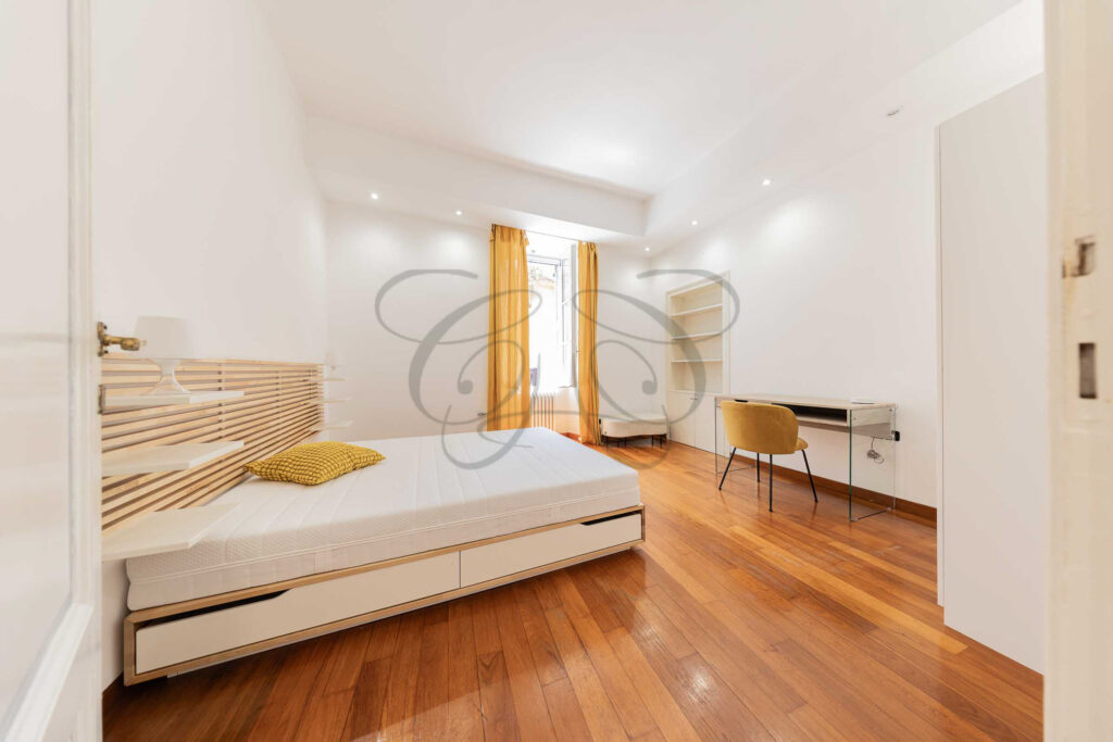 Camera da letto matrimoniale nel Rione Monti con testiera in legno chiaro, letto bianco e pavimento in cotto.