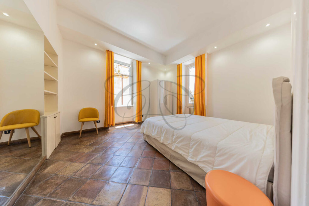 Camera da letto matrimoniale nel Rione Monti con testiera in legno chiaro, letto bianco e pavimento in cotto.