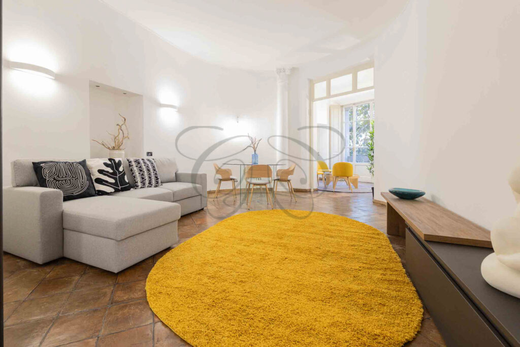 Soggiorno grande e luminoso nel Rione Monti con divano, tappeto giallo e tavolo da pranzo, colonne decorative.