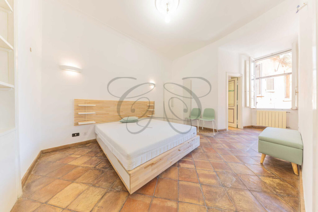 Camera da letto matrimoniale nel Rione Monti con testiera in legno chiaro, letto bianco e pavimento in cotto.