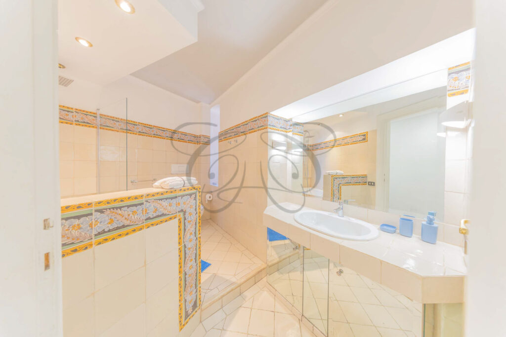 Bagno con pavimento in cotto e pareti rivestite in maiolica artigianale colorata, lavabo classico.