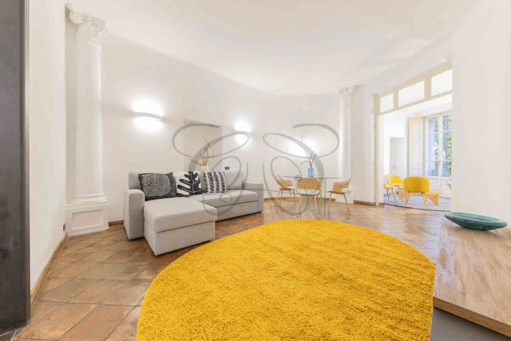 Ampio salone nel Rione Monti con divano, zona pranzo e pavimento in cotto, in un palazzo storico ristrutturato.