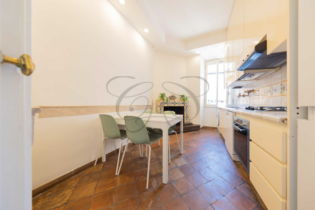 Cucina bianca con tavolo e sedie, pavimento in cotto e camino decorato nel Rione Monti.