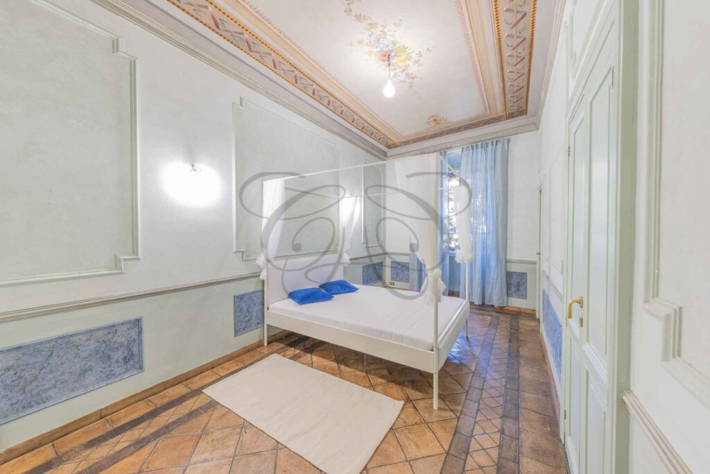 Camera da letto matrimoniale nel Rione Monti con testiera in legno chiaro, letto bianco e pavimento in cotto.