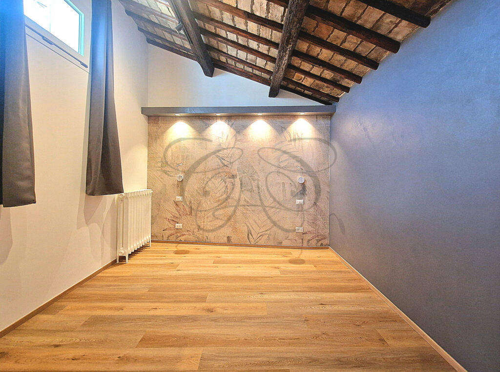 The master bedroom of the attic apartment for rent in Rome, with a decorative wall and exposed wooden ceiling beams.