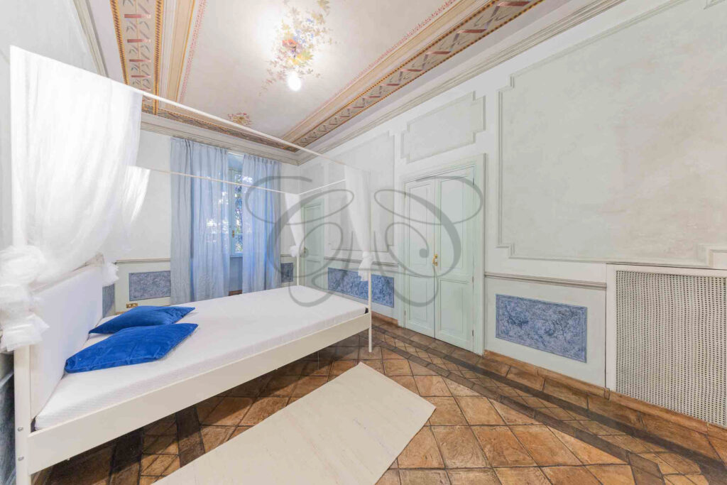 Camera da letto matrimoniale nel Rione Monti con testiera in legno chiaro, letto bianco e pavimento in cotto.