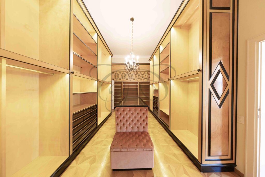 Lussuosa cabina armadio su misura con scaffalature in legno e illuminazione integrata, immobile di prestigio a Roma Parioli.