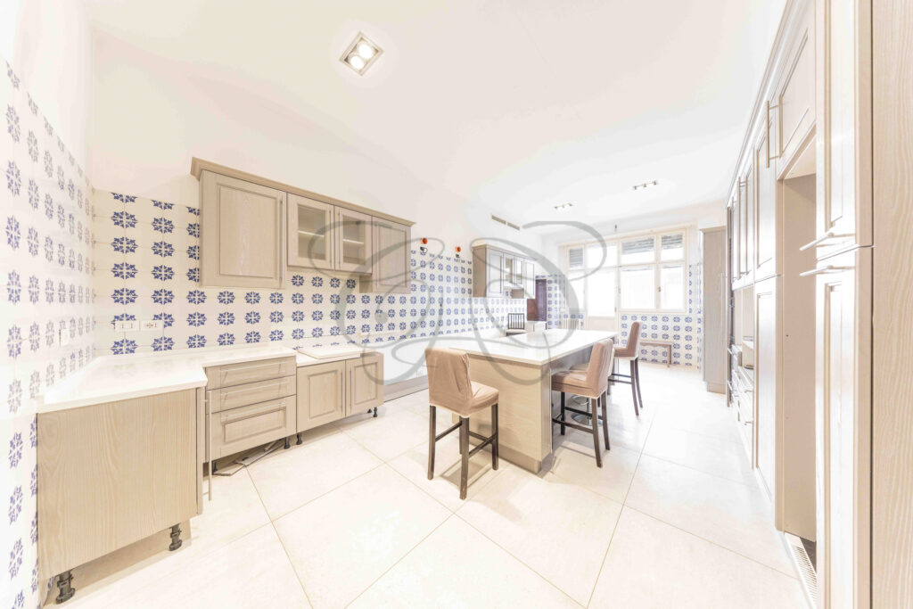 Grande cucina abitabile con isola centrale, arredi bianchi e zona pranzo in un appartamento di lusso a Roma Parioli.