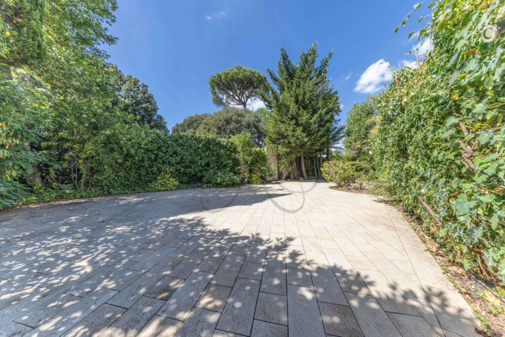 Grande terrazzo pavimentato circondato da una fitta vegetazione, parte di una proprietà di lusso in vendita a Roma Parioli.