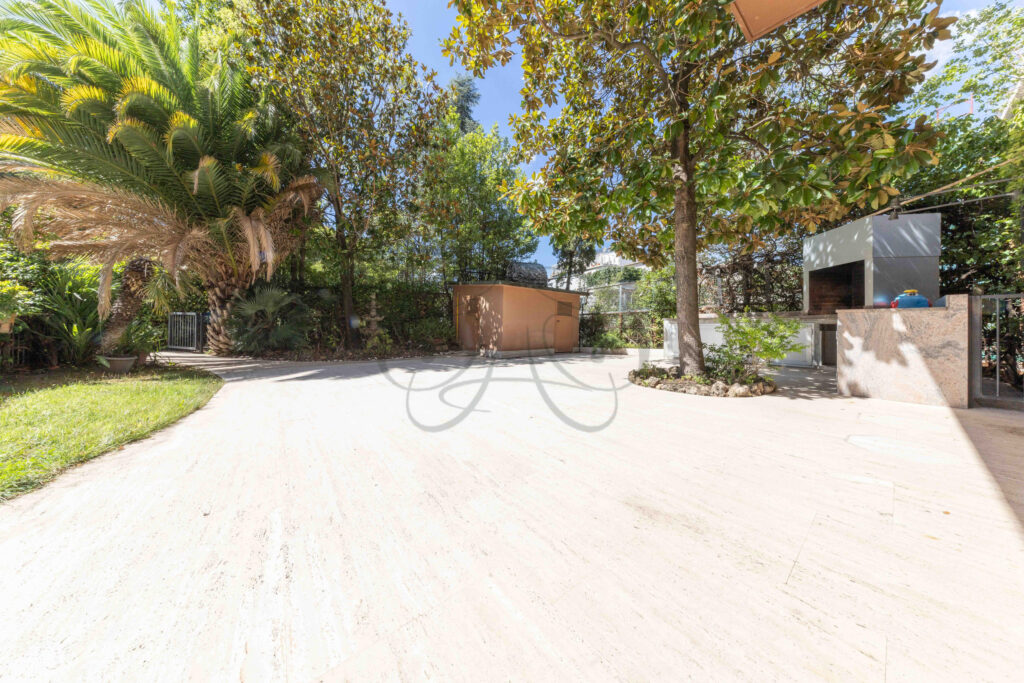 Angolo del terrazzo con barbecue in muratura e vegetazione lussureggiante in una villa di lusso a Roma Parioli.