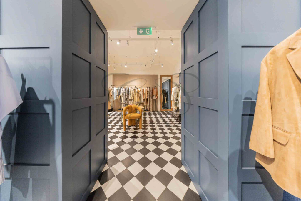 A wide-angle view of a luxury retail space for sale, featuring a checkerboard floor and modern lighting, located in Rome's Tridente.