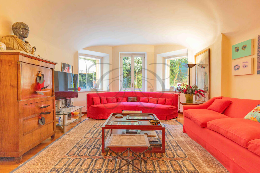Living room with large red sofa and bow window overlooking the garden - Class & Country Homes.